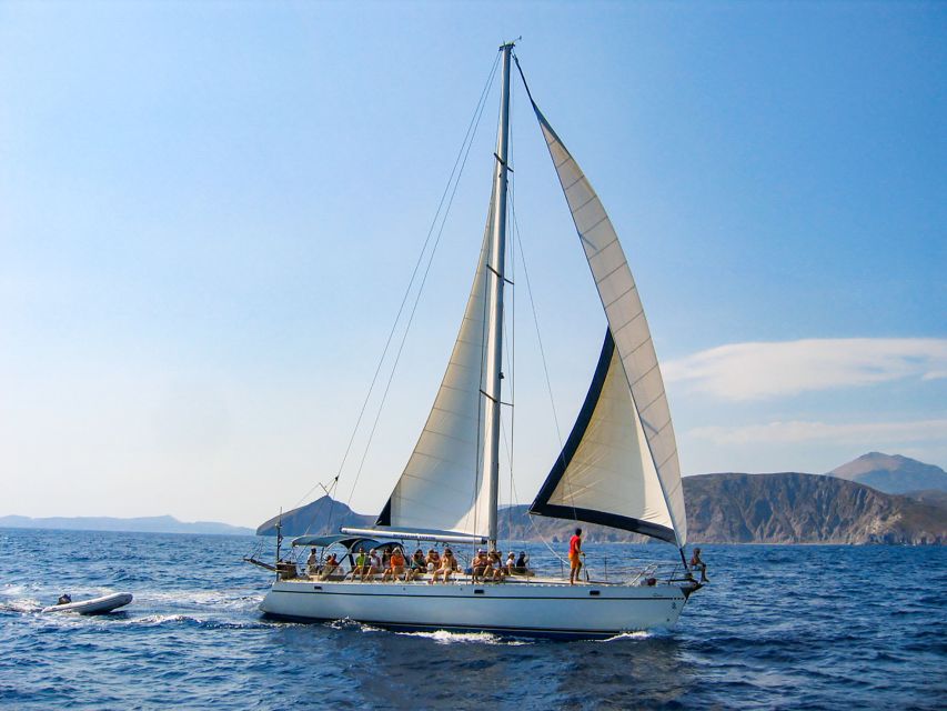 A sailing yacht under full sail off a Cyclades headland